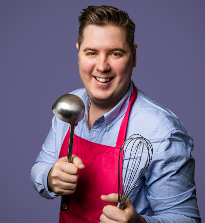 Ben wearing apron holding kitchen utensils